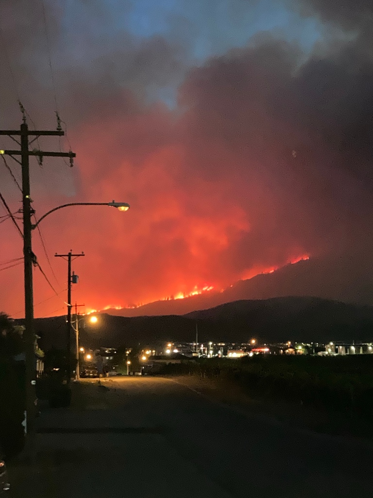 Wildfire at night. The mountain is lit up. Lights from a town are below.