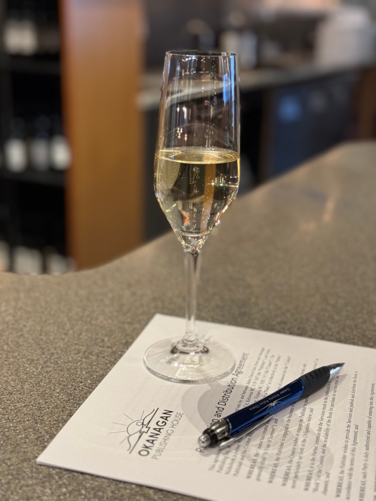 Glass of sparkling wine on book publishing contract with pen.