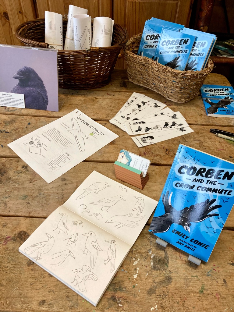Detail, display table for book launch event. Includes book Corben and the Crow Commute by Emily Lonie, plus sketchbook showing concepts for the book’s illustrations. 